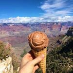 A hand holds a chocolate ice cream cone up against the backdrop of the Grand Canyon